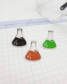 three different colored flasks sitting on top of a white table next to a ruler