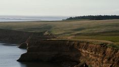 a large body of water sitting on top of a lush green field next to a cliff