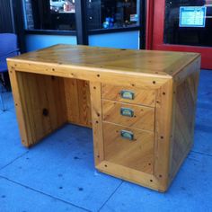 a wooden desk sitting on top of a blue sidewalk next to a building with windows