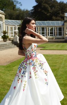 a woman in a white dress standing on grass with her arms behind her head and looking off to the side