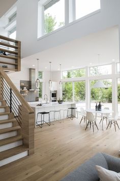 a living room filled with furniture and lots of windows next to a staircase leading up to a kitchen