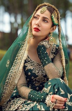 a woman in a green and gold bridal outfit sitting down with her hand on her chin