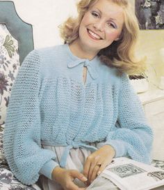 a woman sitting on top of a bed next to a blue chair and holding a magazine