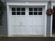 two white garage doors with wreaths on the top and bottom, in front of a blue house