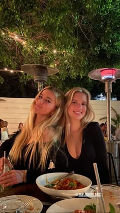 two women sitting at a table with plates of food