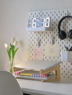 a white desk with headphones on it next to a wall mounted clock and notepads