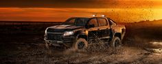 a pickup truck driving through mud in the desert at sunset or dawn with its lights on