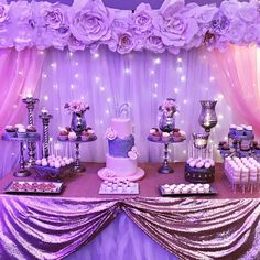 a table topped with lots of cakes and cupcakes next to a purple curtain