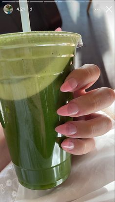 a woman's hand holding a green smoothie in a cup