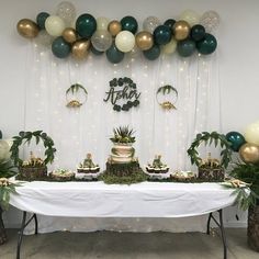 a table topped with lots of cake and desserts covered in green, white and gold balloons