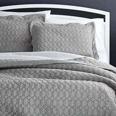 a bed with grey bedspread and pillows on top of the headboard in a bedroom