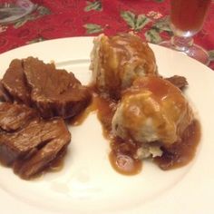 some meat and gravy on a plate next to a glass of beer with a red table cloth