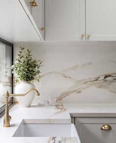 a white kitchen with marble counter tops and gold faucets on the sink area