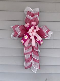 a pink and white flower hanging on the side of a house with ribbon attached to it