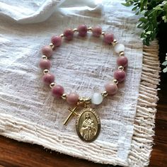 Aquí se presenta una pulsera de rosario elástica hecha con cuentas de piedra de rodocrosita rosa de 8 mm, adornada con un crucifijo en tono dorado y una medalla de Santa Teresa. Se adapta a muñecas de adultos de 6,5 a 7,25 pulgadas. ¡Este artículo está listo para regalar! Se envía con una bolsa con Pink Adjustable Rosary Bracelet For Healing, Adjustable Pink Rosary Bracelet For Healing, Pink Spiritual Gemstone Beads Stretch Bracelet, Spiritual Pink Hand-strung Stretch Bracelet, Pink Spiritual Stretch Bracelet With Round Beads, Spiritual Pink Stretch Bracelet With Round Beads, Pink Rosary Bracelet With Round Beads For Healing, Spiritual Pink Charm Bracelet With Round Beads, Pink Hand-strung Spiritual Rosary Bracelet