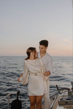 a man and woman standing on the deck of a boat in the ocean at sunset