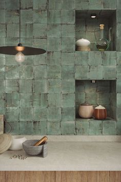 a kitchen with green tiles on the wall and wooden shelves in the center, along with various pots and bowls