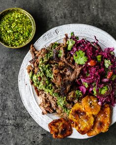 a white plate topped with meat and veggies next to a bowl of pesto