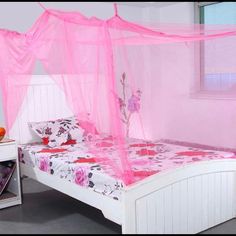 a bed with pink netting over it and flowers on the bedspread, in front of a window