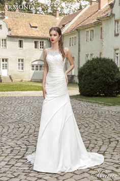 a woman in a white wedding dress standing on a cobblestone road with her hands on her hips