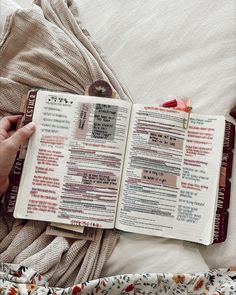 an open book on top of a bed next to a person holding a cell phone