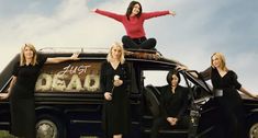 four women standing on top of a car in front of a sign that says, they are dead