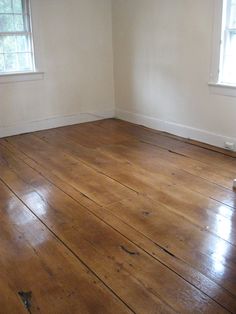 an empty room with wood floors and two windows