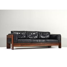 a black leather couch sitting on top of a wooden table next to a white wall