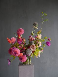 a vase filled with lots of colorful flowers on top of a wooden table next to a gray wall