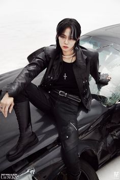 a man sitting on the hood of a car with his hands in his pockets and wearing all black