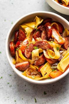 two bowls filled with pasta and sausages on top of a white countertop next to each other