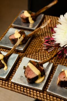 four square plates with food on them sitting on a table next to a white flower