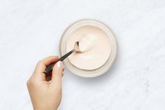 a person holding a spoon in a bowl with cream on it and another hand reaching for something