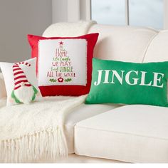 two christmas pillows sitting on top of a white couch next to a red and green pillow