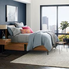 a bed room with a neatly made bed next to a large window and a painting on the wall