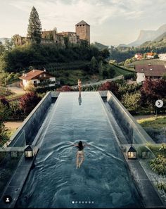 a woman swimming in a large pool surrounded by lush green hills and houses on the other side