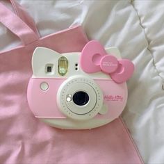 a pink hello kitty camera laying on top of a bed next to a pink bag