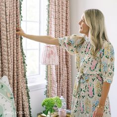 a woman standing in front of a window pointing at something on the wall behind her