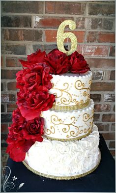 a white and gold wedding cake with red flowers on the bottom tier, number six