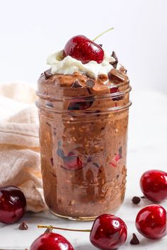 a jar filled with chocolate pudding and cherries on top of a table next to some strawberries