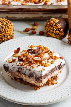 a piece of cake on a plate with nuts around it and another dessert in the background