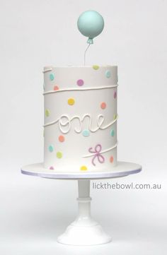 a white cake with polka dots on it and a balloon floating from the top that says one