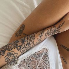 a woman laying on top of a bed with tattoos on her arm and leg next to a pillow