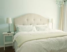 a white bed sitting in a bedroom next to a window with curtains on both sides