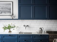 a kitchen with blue cabinets and white subway backsplash, stainless steel appliances and an art print on the wall