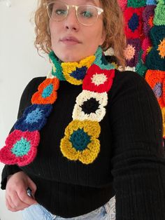 a woman wearing glasses and a crocheted scarf is standing in front of a wall