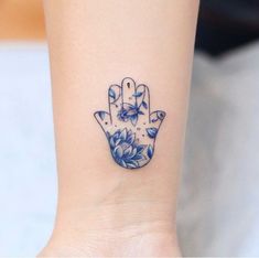 a small blue and white flowered tattoo on the wrist with a hamsa hand