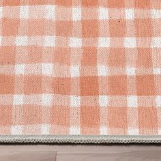 an orange and white checkered rug on top of a wooden floor next to a cat