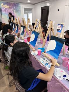 a group of people sitting around a table with paintings on it and paintbrushes in front of them