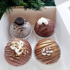 four chocolate cupcakes in a box with white frosting and decorations on top